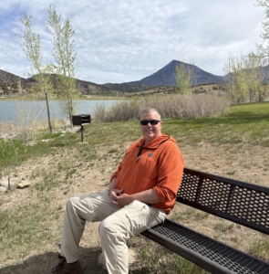 Paul Aspelin sitting on a bench in Crawford State Park in front of the Crawford Reservoir