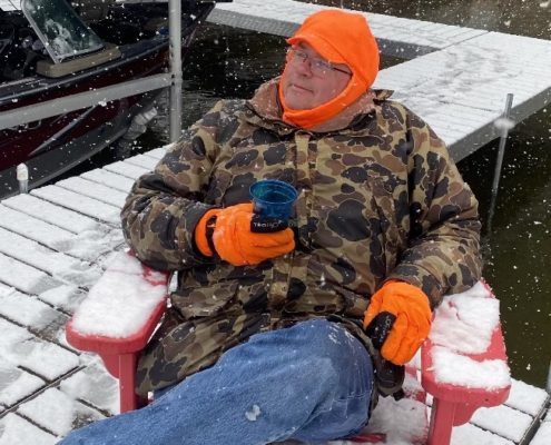 Paul Aspelin sitting in his winter jacket on the fishing dock while it's snowing