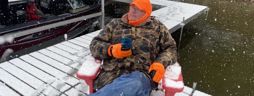 Paul Aspelin sitting in his winter jacket on the fishing dock while it's snowing