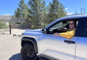 Rocky Mountain National Park entrance sign with Paul waving from the 4Runner parked in front of the sign