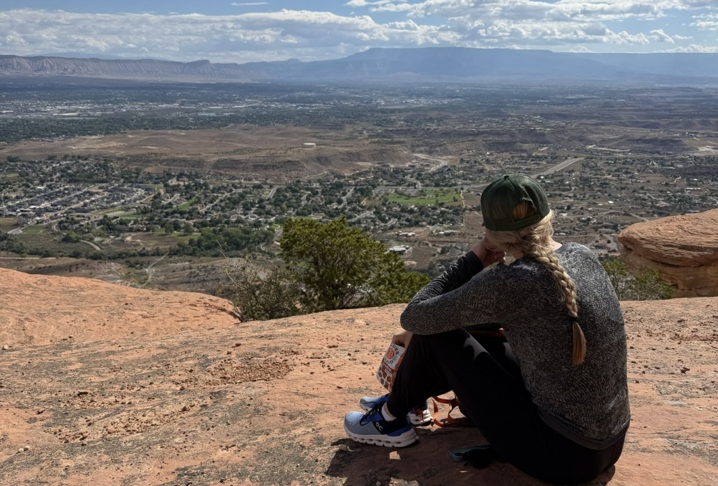 10-Day Grand Junction Challenge Megan Jirele Writer sitting on slickrock looking out over the valley towards Grand Junction