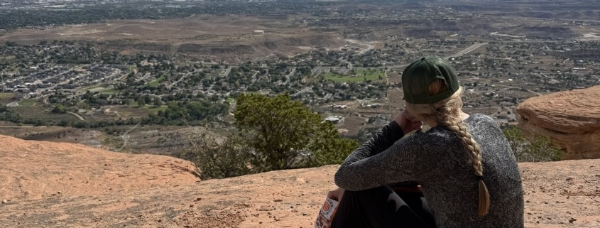 10-Day Grand Junction Challenge Megan Jirele Writer sitting on slickrock looking out over the valley towards Grand Junction