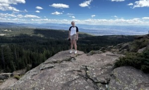 Megan on top of rocks on the Land o' Lakes trail on the Grand Mesa with expansive mountain views behind her