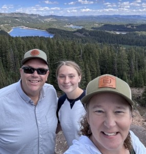 Paul Megan and Michelle Aspelin standing on a rock at the top of the Grand Mesa with alpine trees and a lake behind us