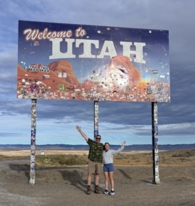 Paul and Megan standing on the side of I-70 at the Welcome to Utah road sign